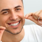 Closeup of young man flossing his teeth. Cleaning teeth with dental floss
