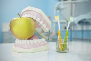 Denture, apple and toothbrushes in glass in dental surgery