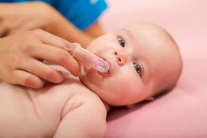 Mother cleaning baby`s mouth with special fingertip brush for children.