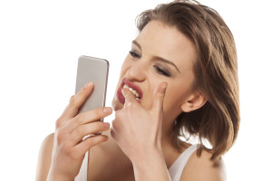 girl cleans stains on her teeth looking in the smartphone