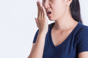 Asian woman checking her breath with her hand on white background.