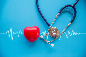 red rubber heart and stethoscope on blue background with cardiogram, health concept