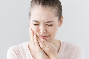 Closeup of beautiful teenage girl isolated on gray background touching her face and closing eyes with expression of horrible suffer from health problem and aching tooth, showing dissatisfaction.